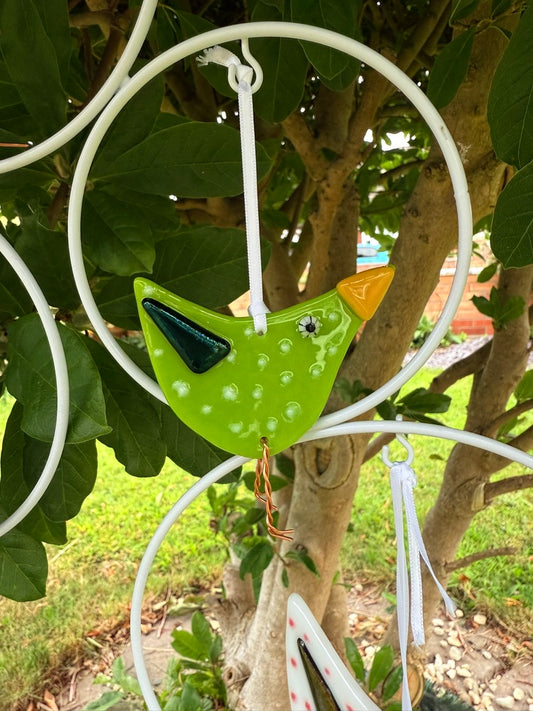 Decorative green bird ornament hanging from a white circular frame against a natural background.