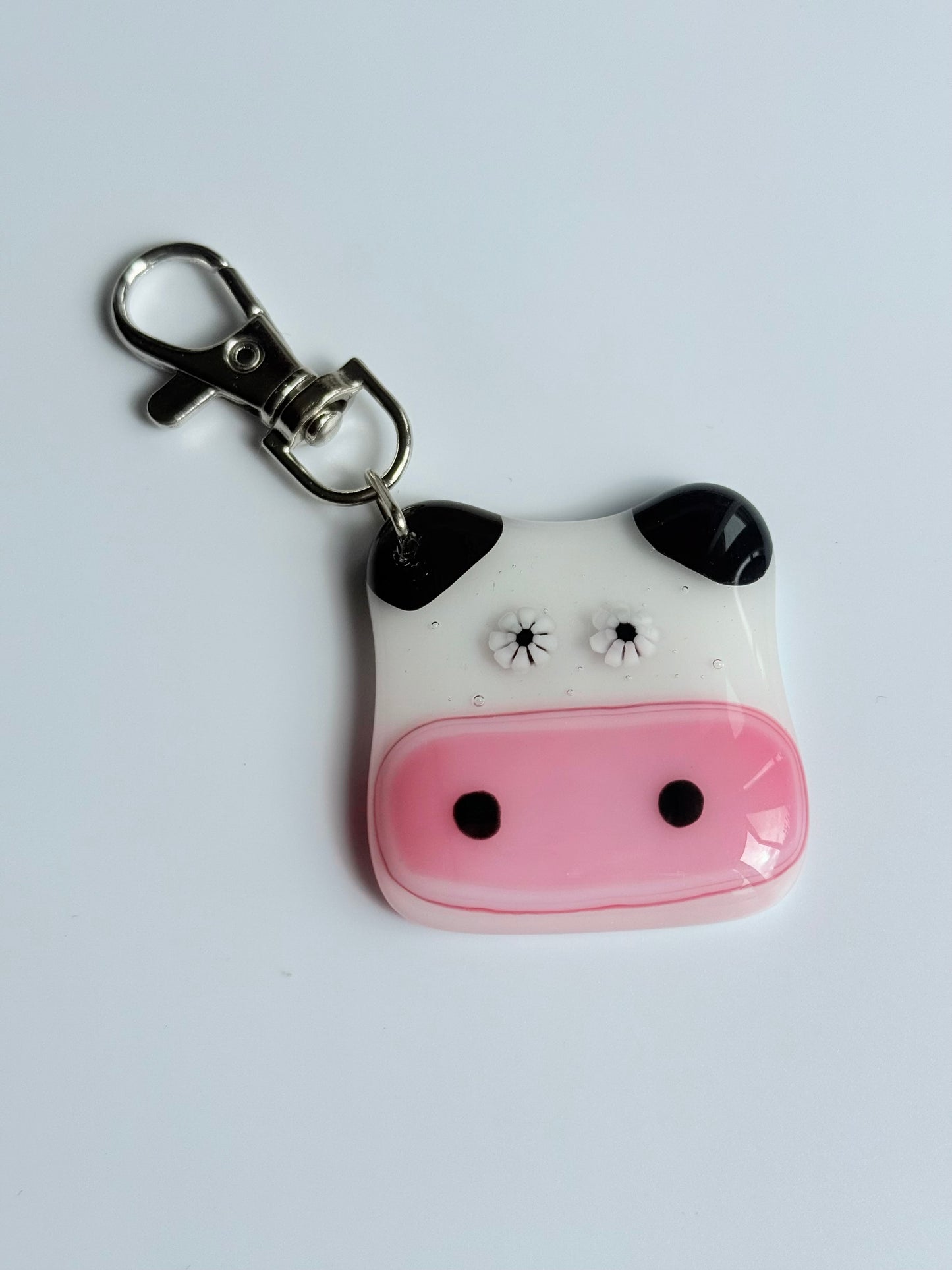 Cow-shaped keychain with a pink face and black spots on a white background