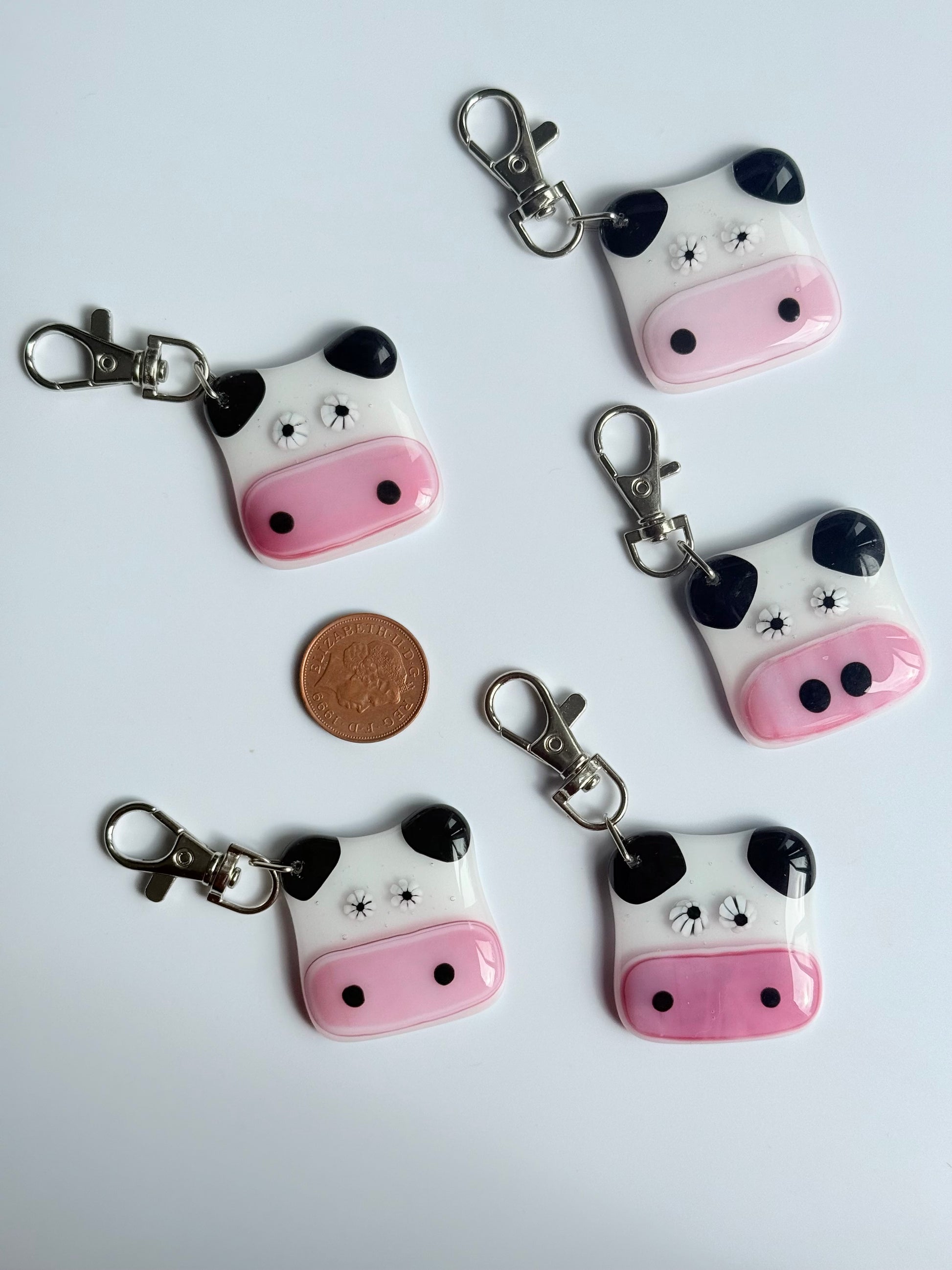 Five cow-shaped keychains with pink faces and black accents on a white background.