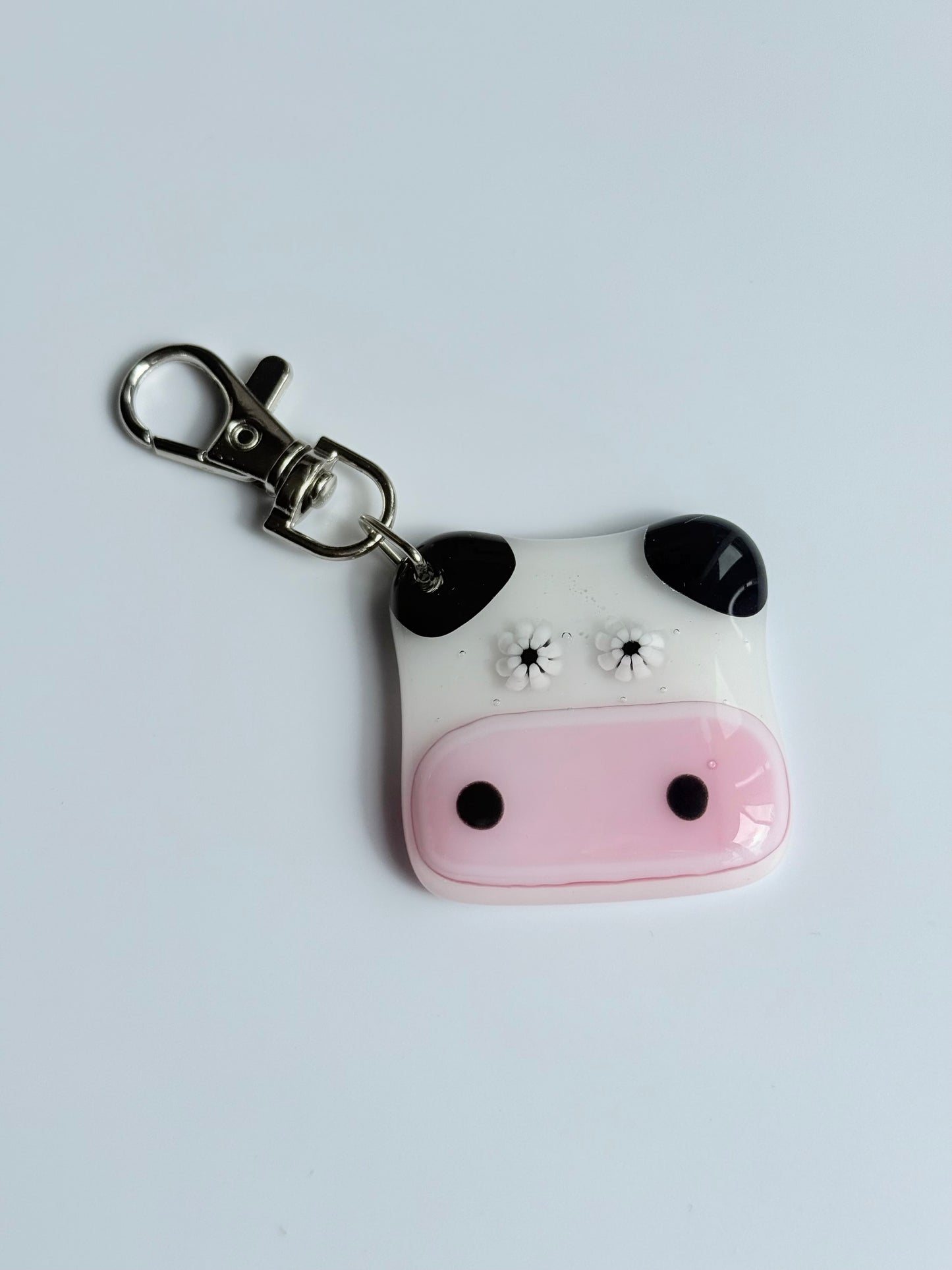 Cow face keychain with a pink nose and black spots on a light gray background